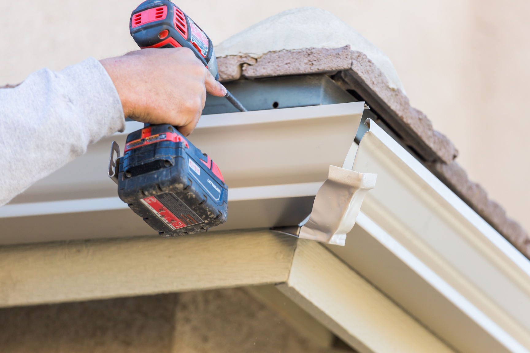 Worker Attaching Aluminum Rain Gutter to Fascia of House.