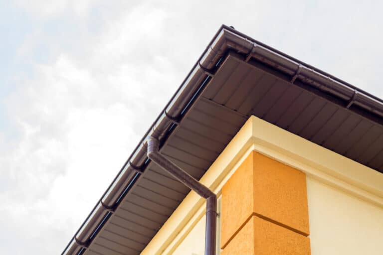 Close up detail of cottage house corner with brown metal planks siding and roof with steel gutter rain system. Roofing, construction, drainage pipes installation and connection concept.